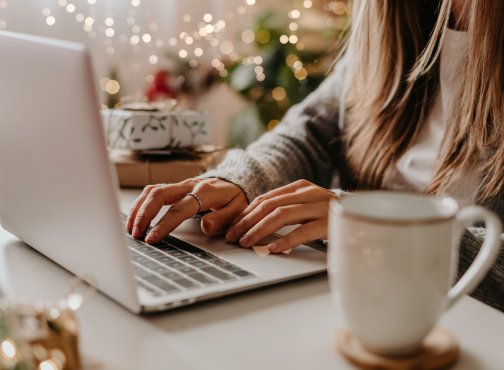woman using a laptop with a string of holiday lights behind her